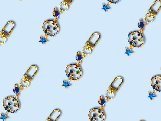 Pastel space cat keychains with lobster claw clasp on blue background.