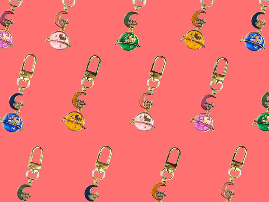 Gold-plated Moon Cats keychain with pastel enamel and lobster clasp on coral background